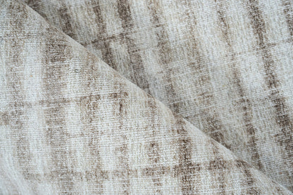 Neutral beige-taupe rug with subtle distressed pattern and soft woven pile, folded corner.