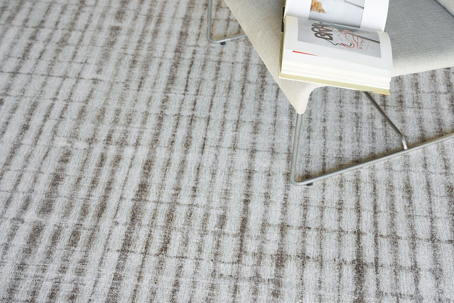 Beige rug with a textured gray striped pattern; an open magazine rests on the rug.