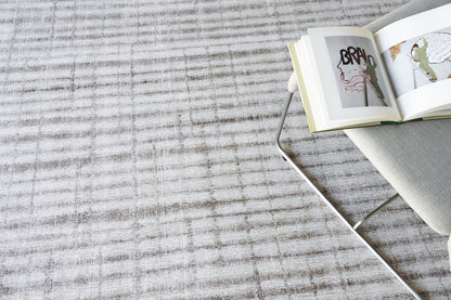 Light grey textured rug with a metal-framed chair and an open art book resting on the chair.