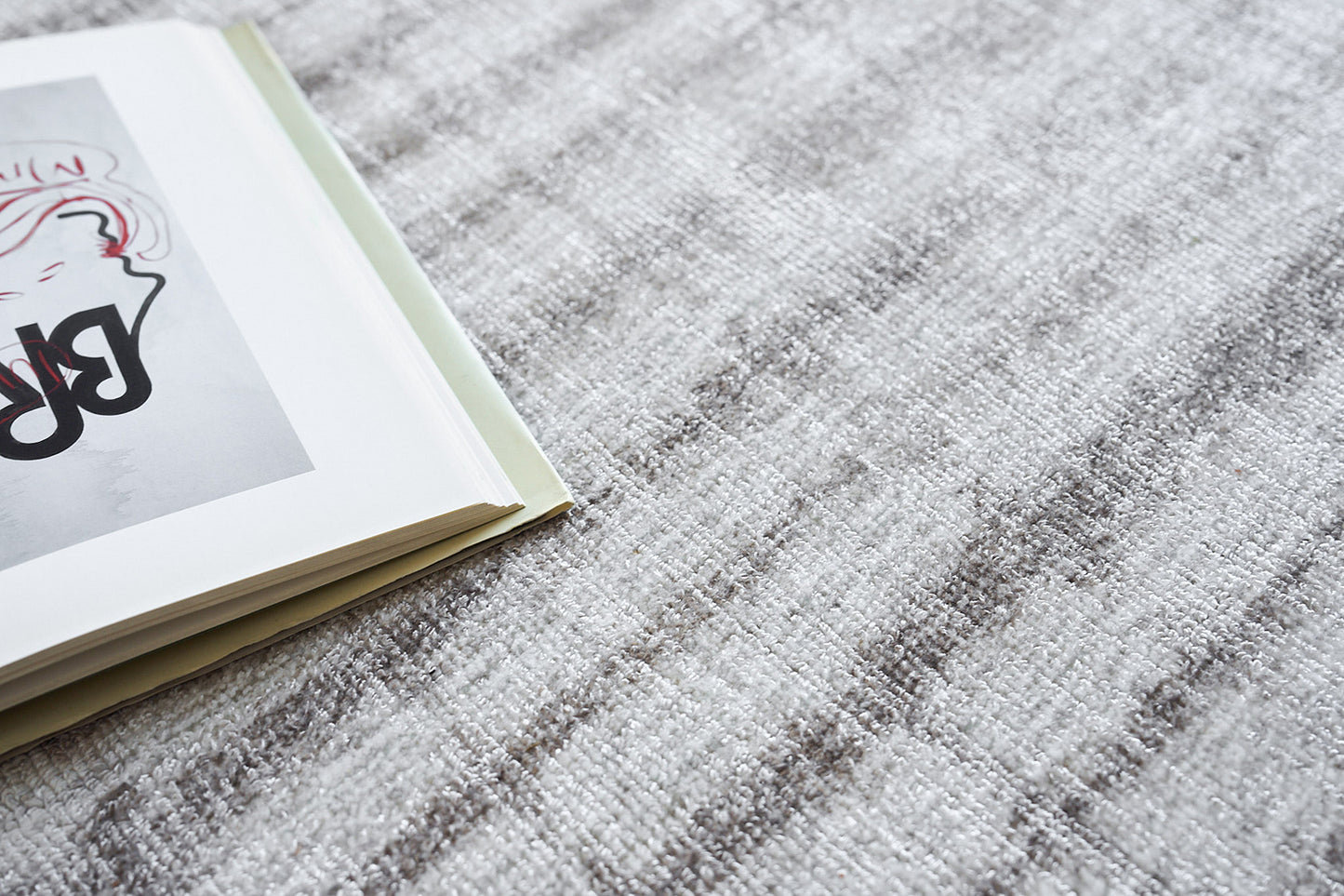 Open magazine with abstract black and pink illustration on pale page, resting on a gray textured rug.