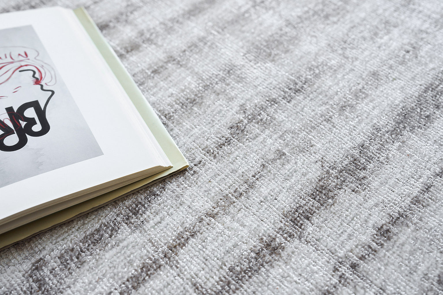 Open magazine with abstract black and pink illustration on pale page, resting on a gray textured rug.