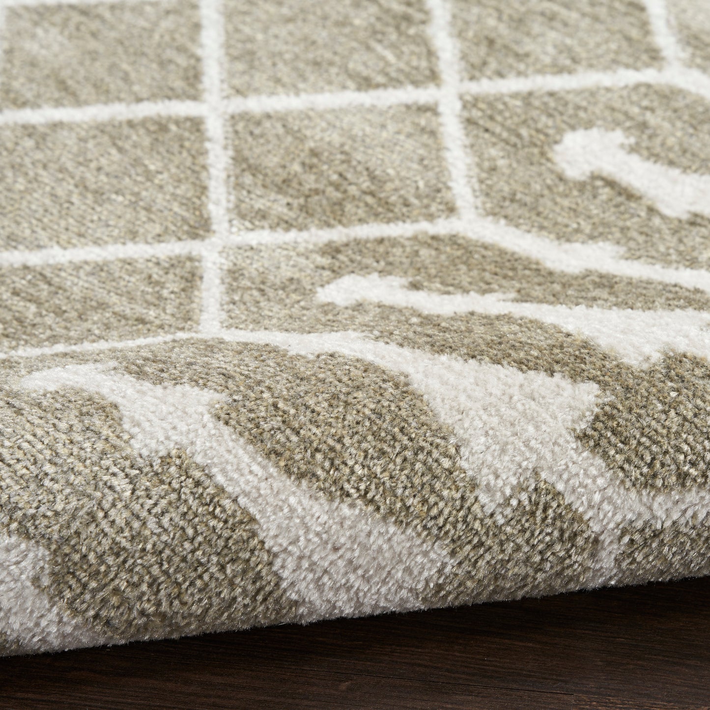 Taupe and white geometric shag rug with grid pattern and wavy lines, rolled edge on dark wood floor.