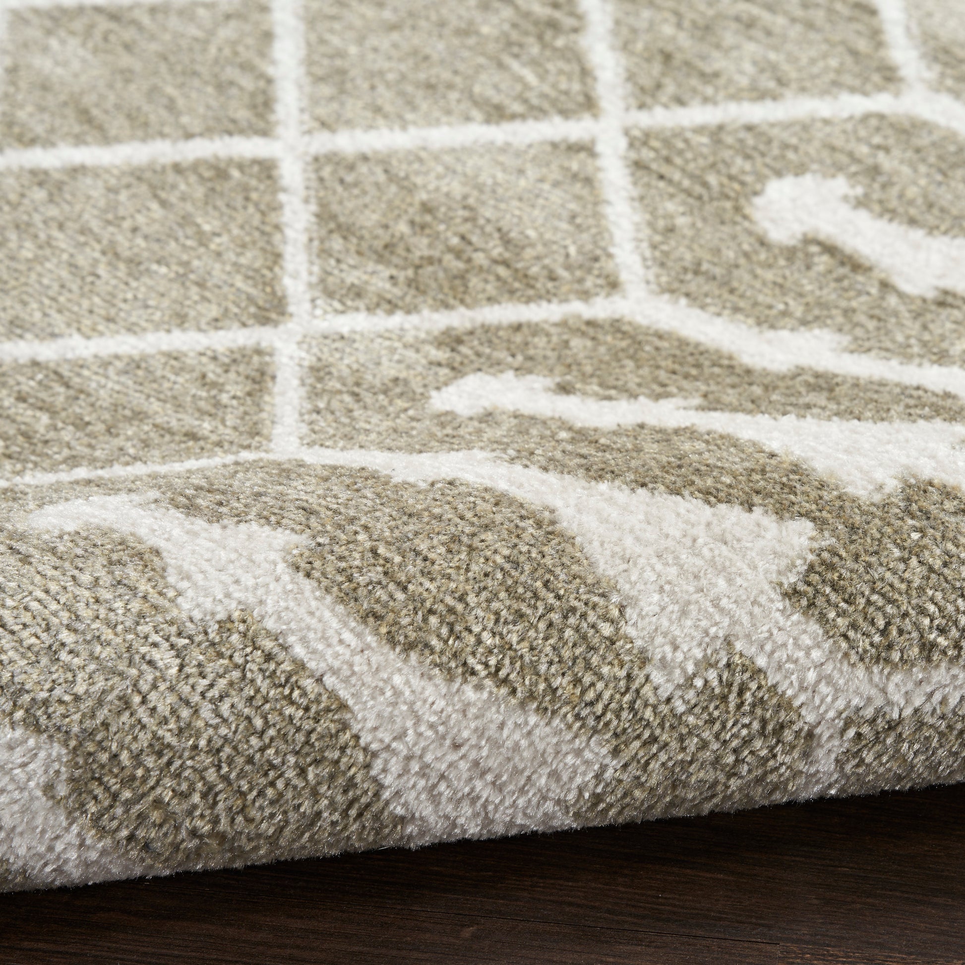 Taupe and white geometric shag rug with grid pattern and wavy lines, rolled edge on dark wood floor.