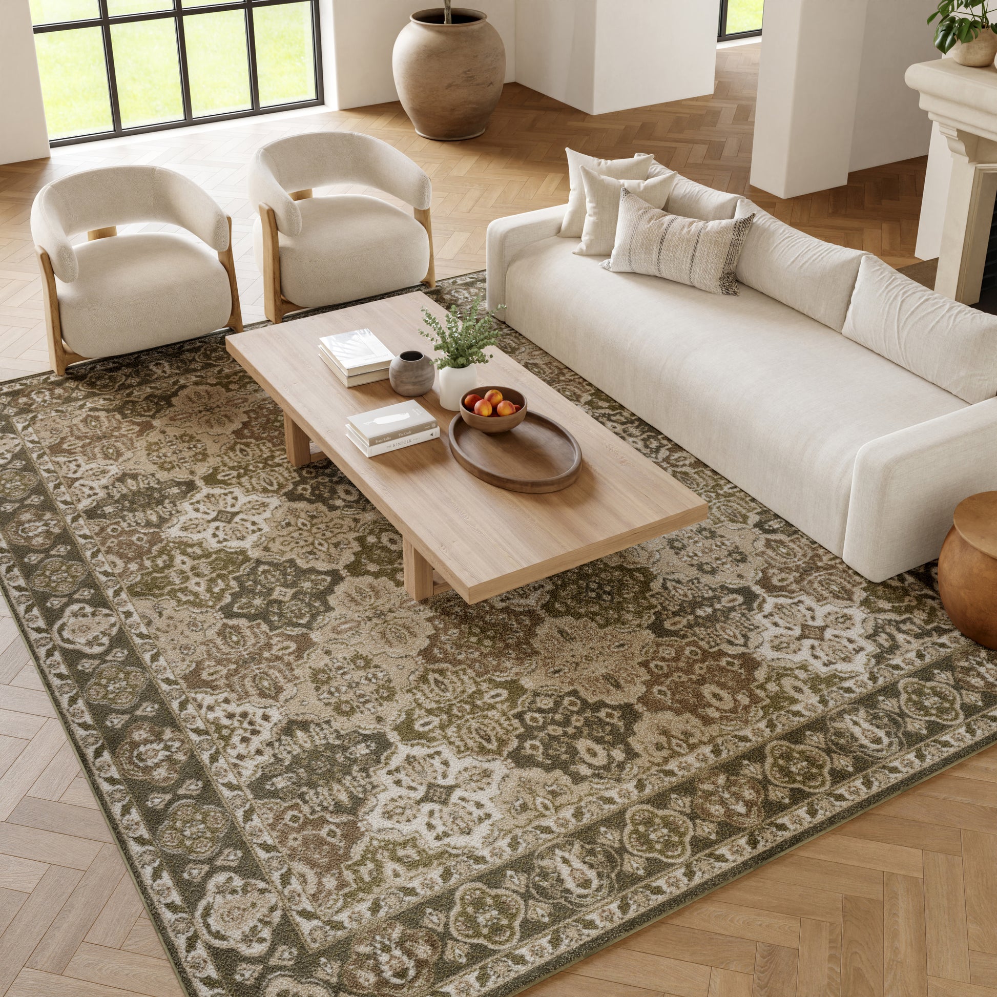 Neutral living room with a light wood rectangular coffee table, cream sofa and armchairs on a patterned gray-green rug.