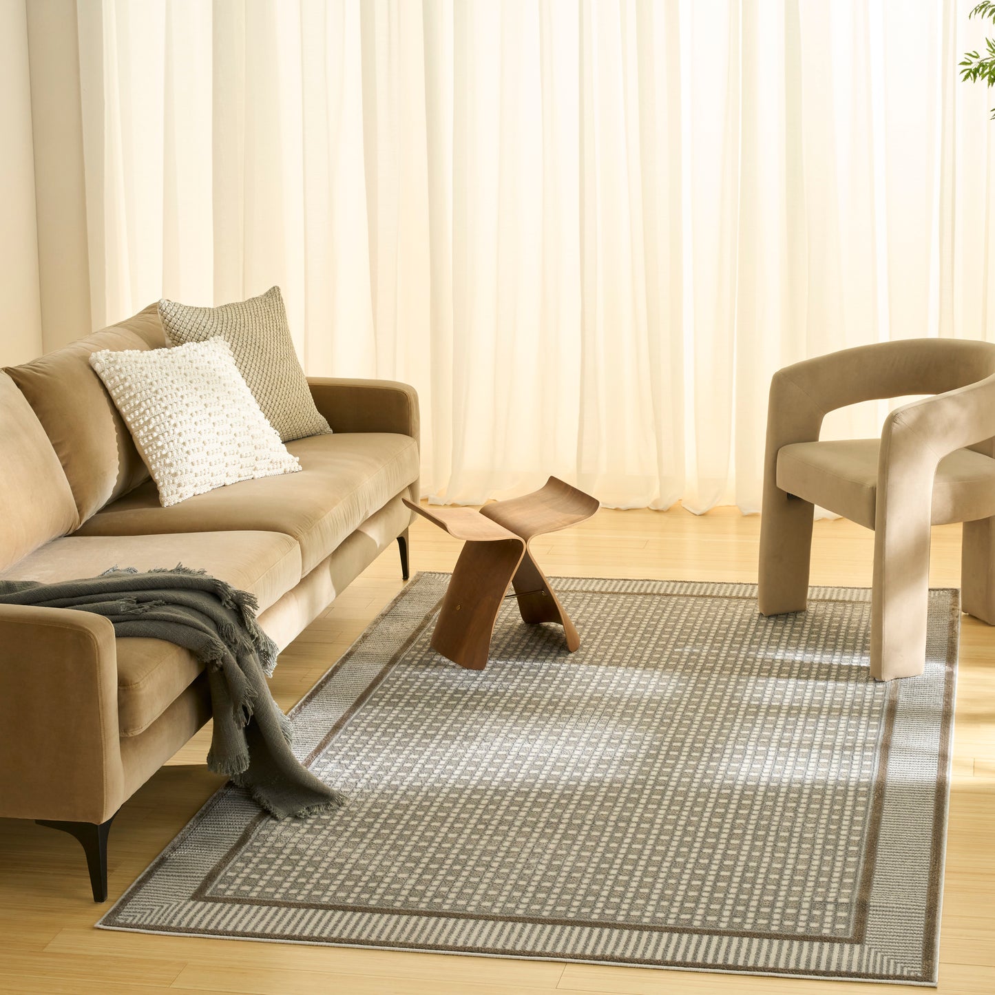 Beige fabric sofa with white textured pillow, gray throw, curved wood coffee table, gray patterned rug, beige armchair and sheer curtains.