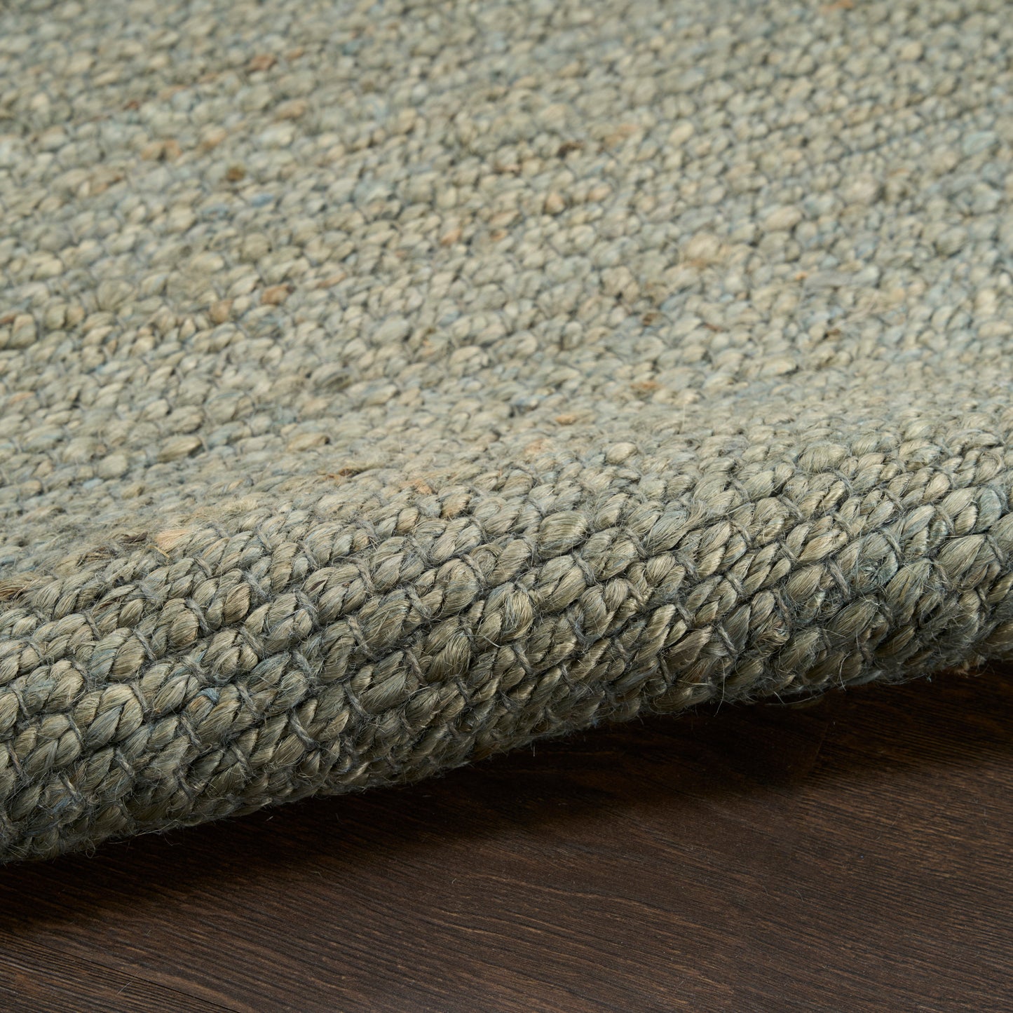 Grey-blue textured loop-pile rug with a chunky braided edge on dark wood floor.