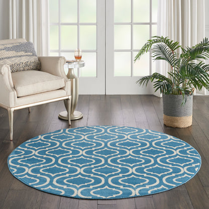 Round blue rug with white wavy pattern in a cozy living room beside a beige armchair & side table & potted plant.