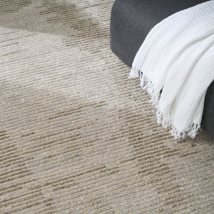 Beige textured rug with subtle horizontal stripes, gray sofa edge and white fringed throw blanket.