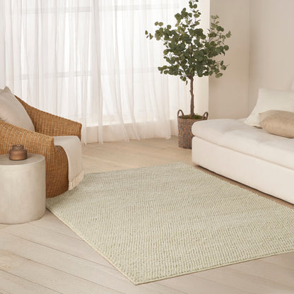 Neutral living room rug on light wood floor with beige sofa, wicker chair, potted tree in woven basket and sheer curtains.