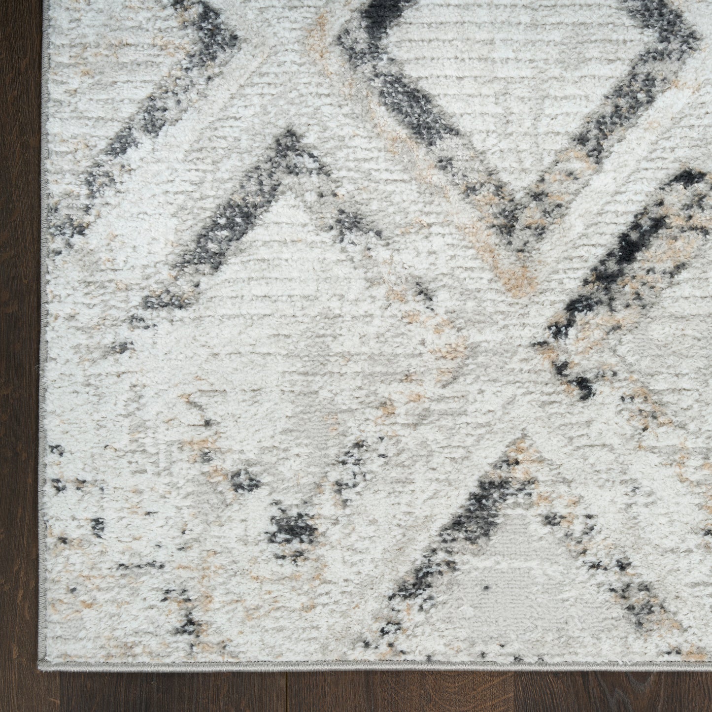 Cream and gray geometric rug with black and tan diamond patterns on dark wood floor.