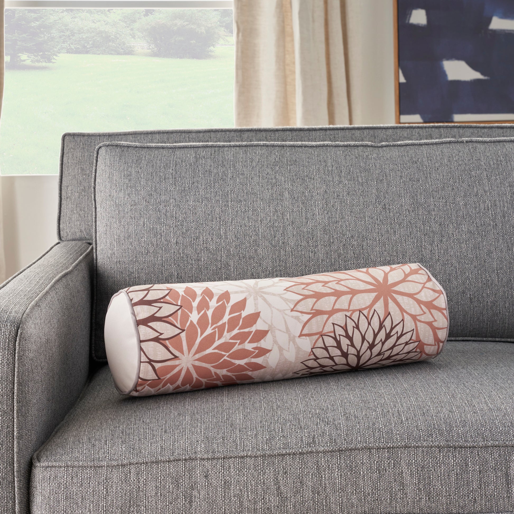 Grey fabric sofa with a cylindrical bolster pillow featuring mandala-style peach and brown floral pattern.