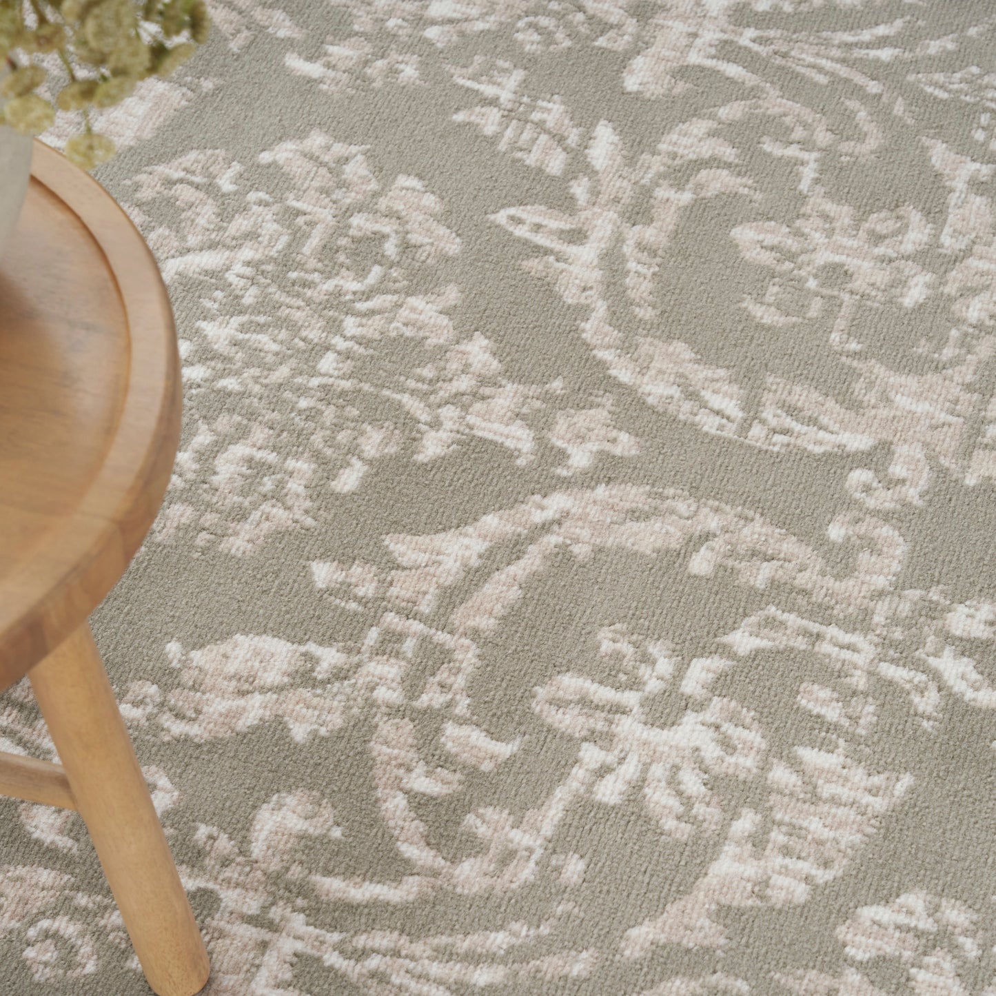 Light taupe rug with white damask floral pattern; partial view of a round light-wood stool.