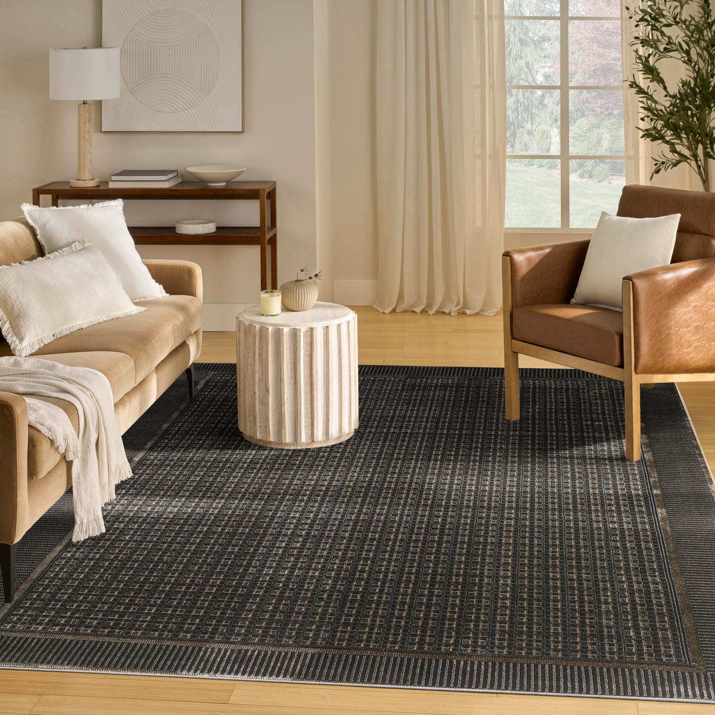 Cozy living room with tan sofa, brown leather armchair, round beige side table, and dark patterned rug.