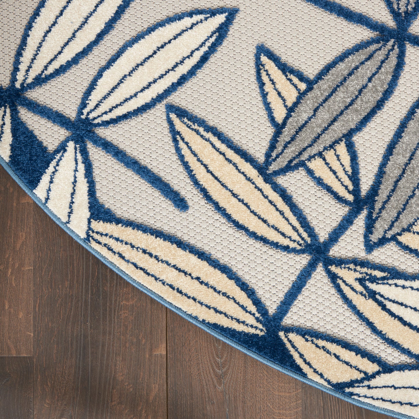 Round rug with blue leaf outlines on beige woven background; blue border, on dark wood floor.