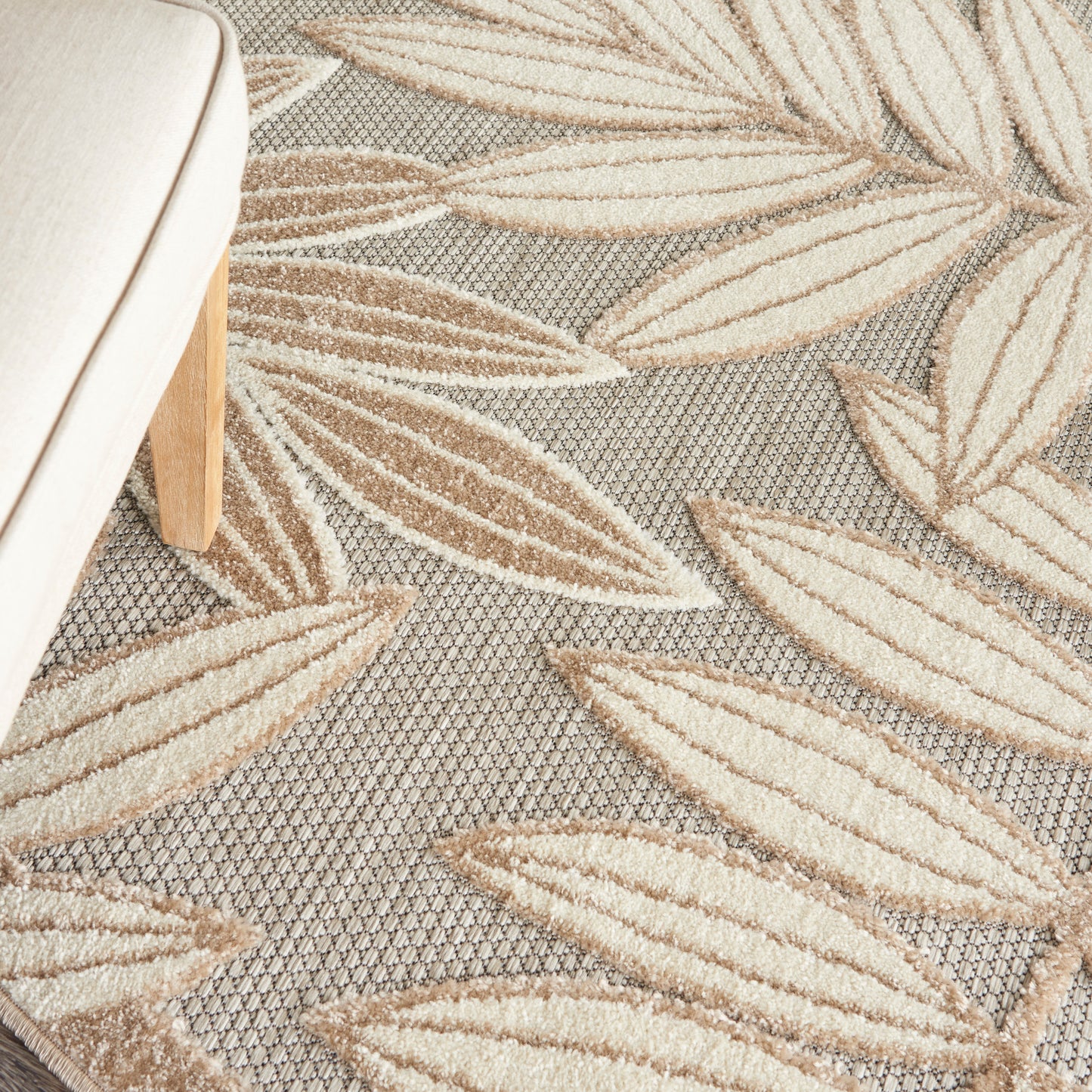 Grey rug with beige leaf motifs in a textured weave; light wood chair leg visible on the left.