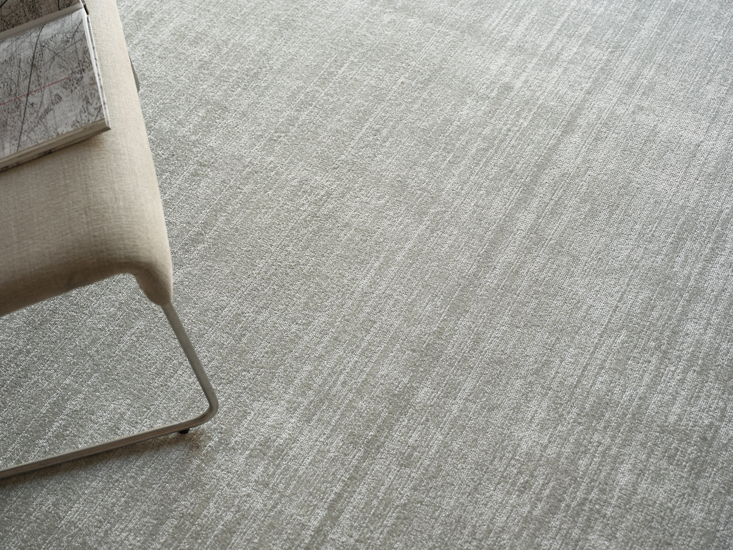 Beige fabric lounge chair with slim metal cantilever frame on light gray textured carpet, modern minimalist style.