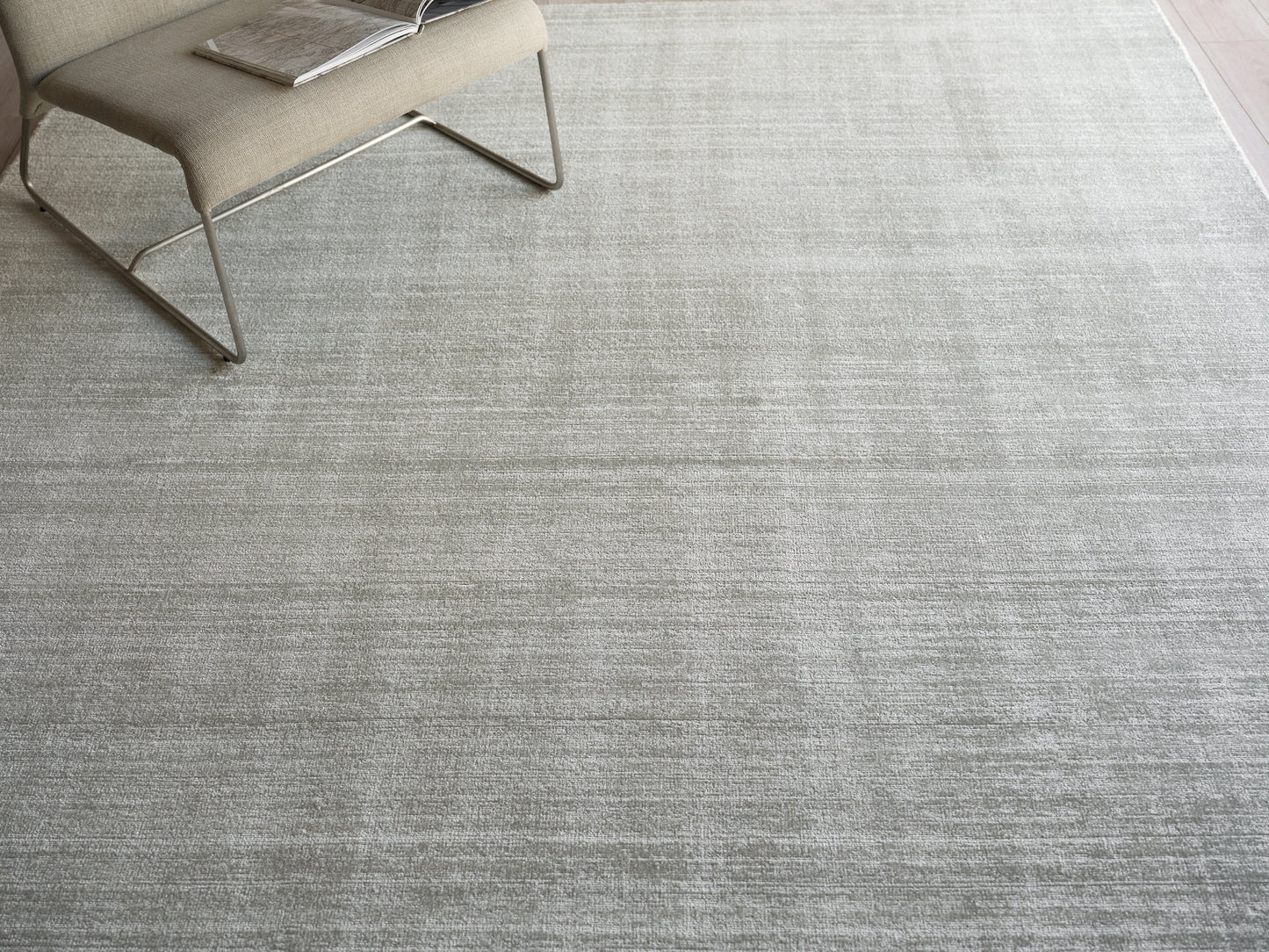 Light gray textured area rug with a beige modern lounge chair and a magazine on the seat.