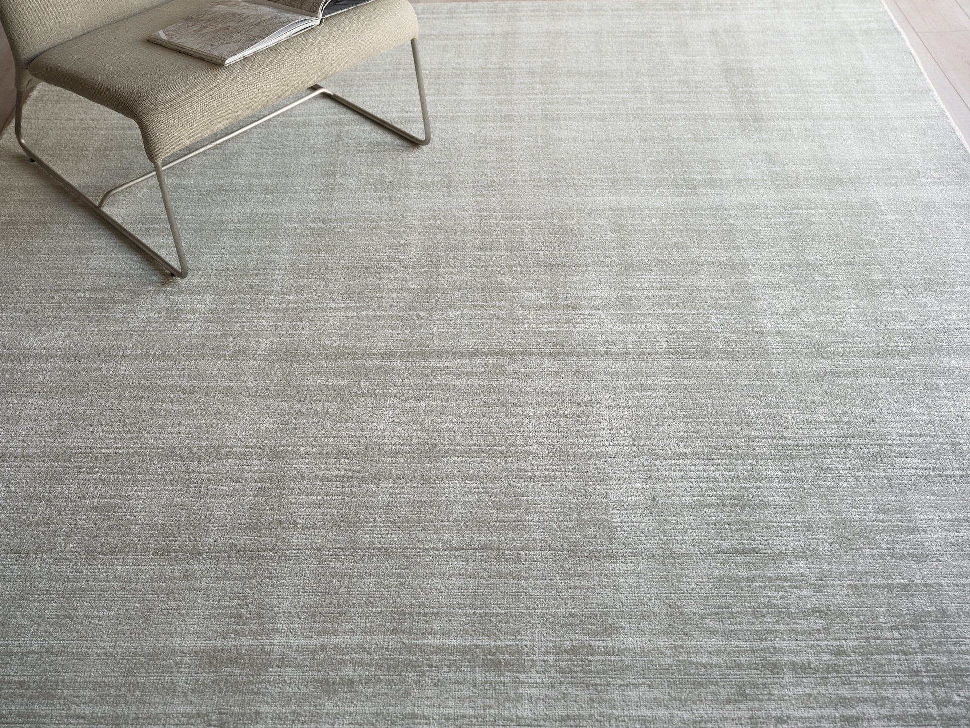 Light gray textured area rug with a beige modern lounge chair and a magazine on the seat.