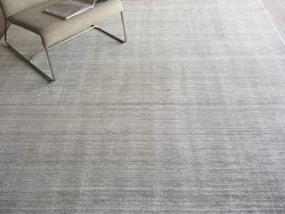 Light gray textured area rug with a beige modern lounge chair and a magazine on the seat.