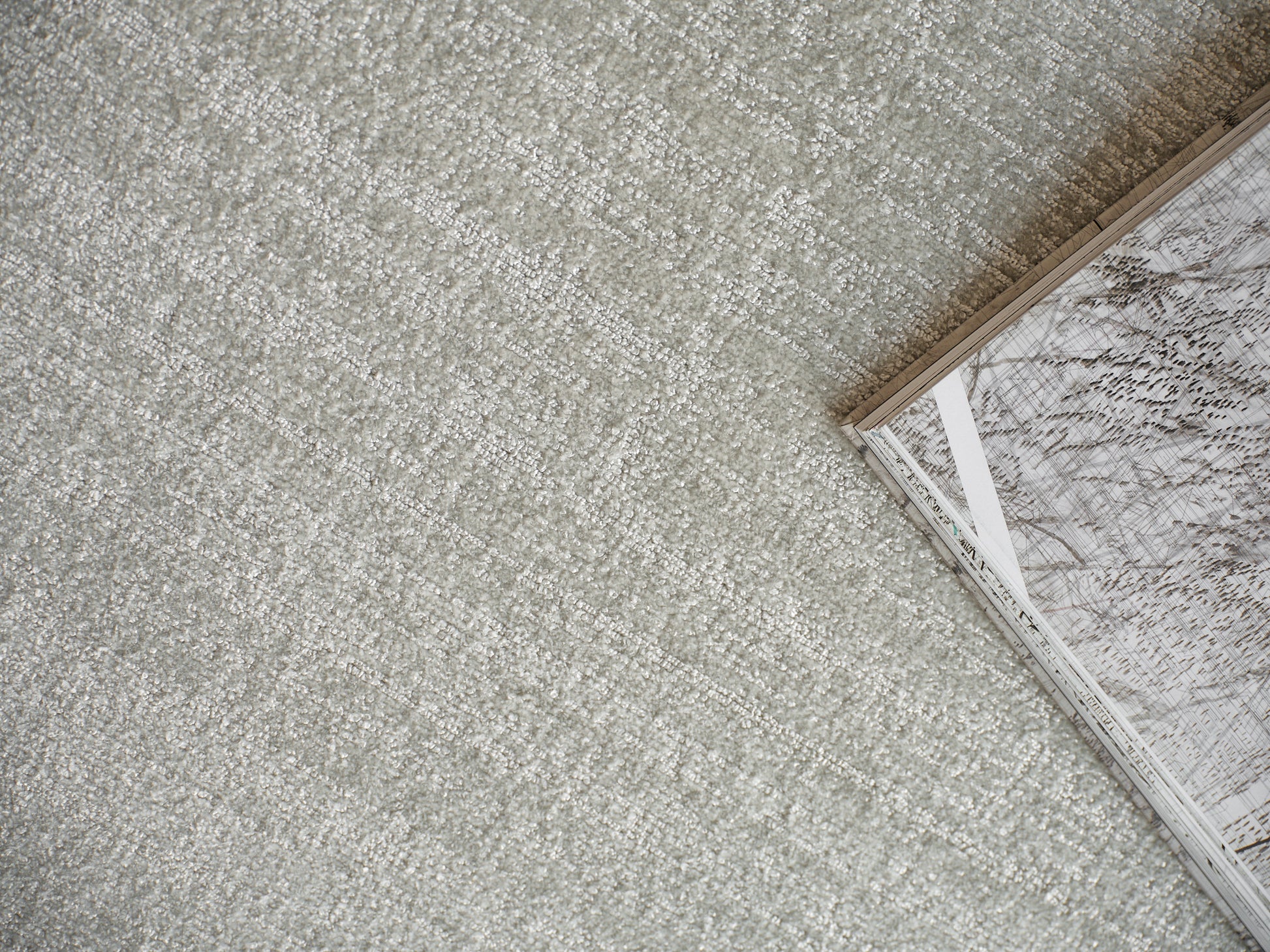 Soft gray textured carpet with a corner-open magazine featuring marble-patterned pages.