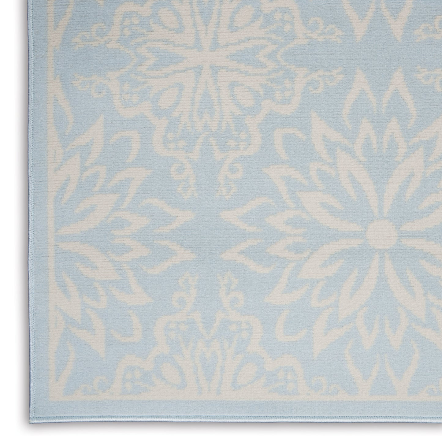 Light blue woven rug with large white snowflake/flower motifs; soft decorative rug with a finished edge
