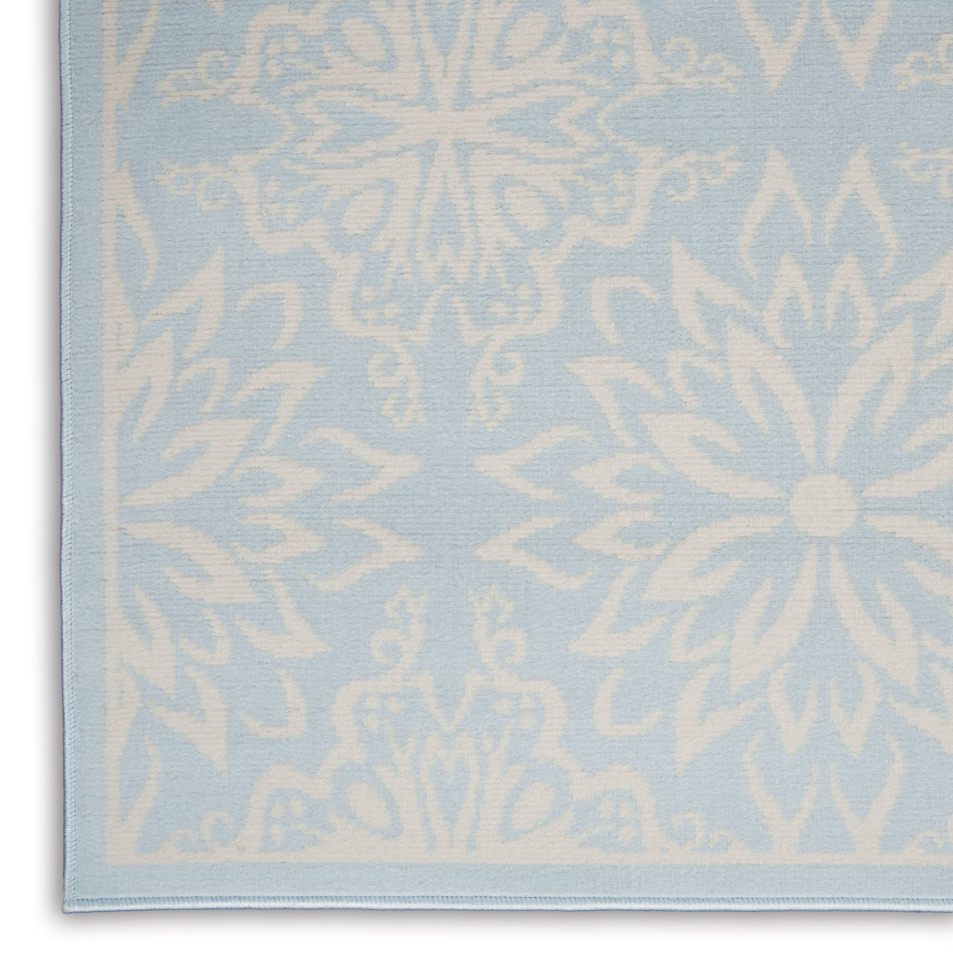 Light blue woven rug with large white snowflake/flower motifs; soft decorative rug with a finished edge