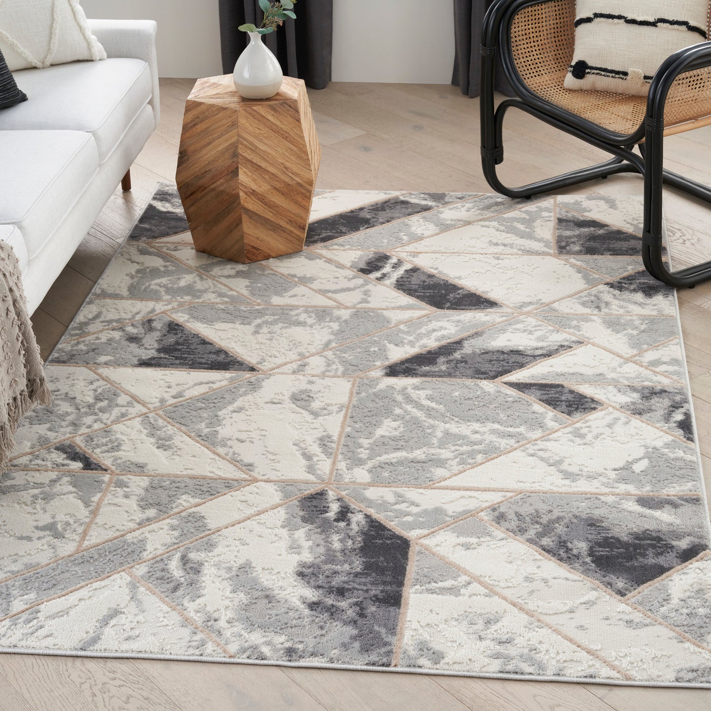 Geometric patterned rug in cream, gray and taupe in a modern living room with a wooden geometric side table and cane chair.