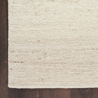 Cream boucle rug with chunky looped texture on dark wood floor, edge visible.