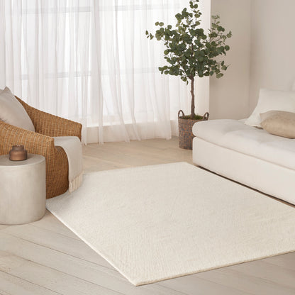 Cream rectangular area rug in a bright living room with white sofa, wicker chair, and potted plant.