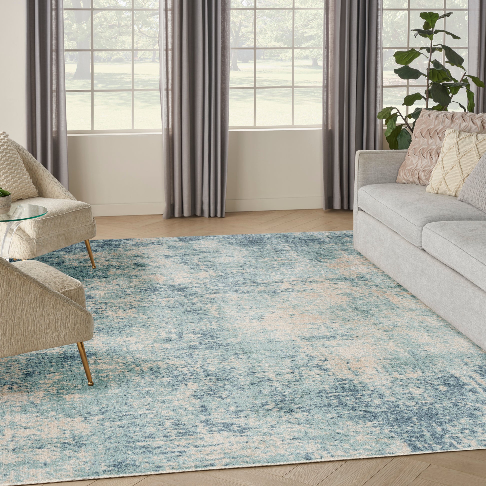 Bright living room with blue abstract area rug, beige accent chairs, gray sofa, glass coffee table, and large windows.