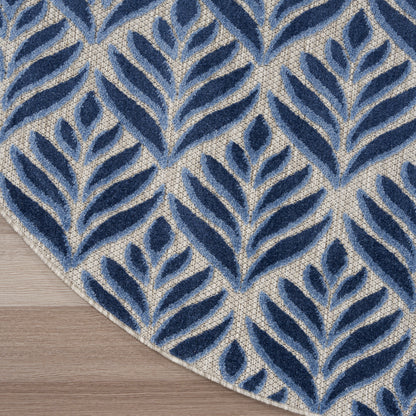 Navy blue tropical leaf-pattern rug, round, on a beige woven background with light wood floor visible.