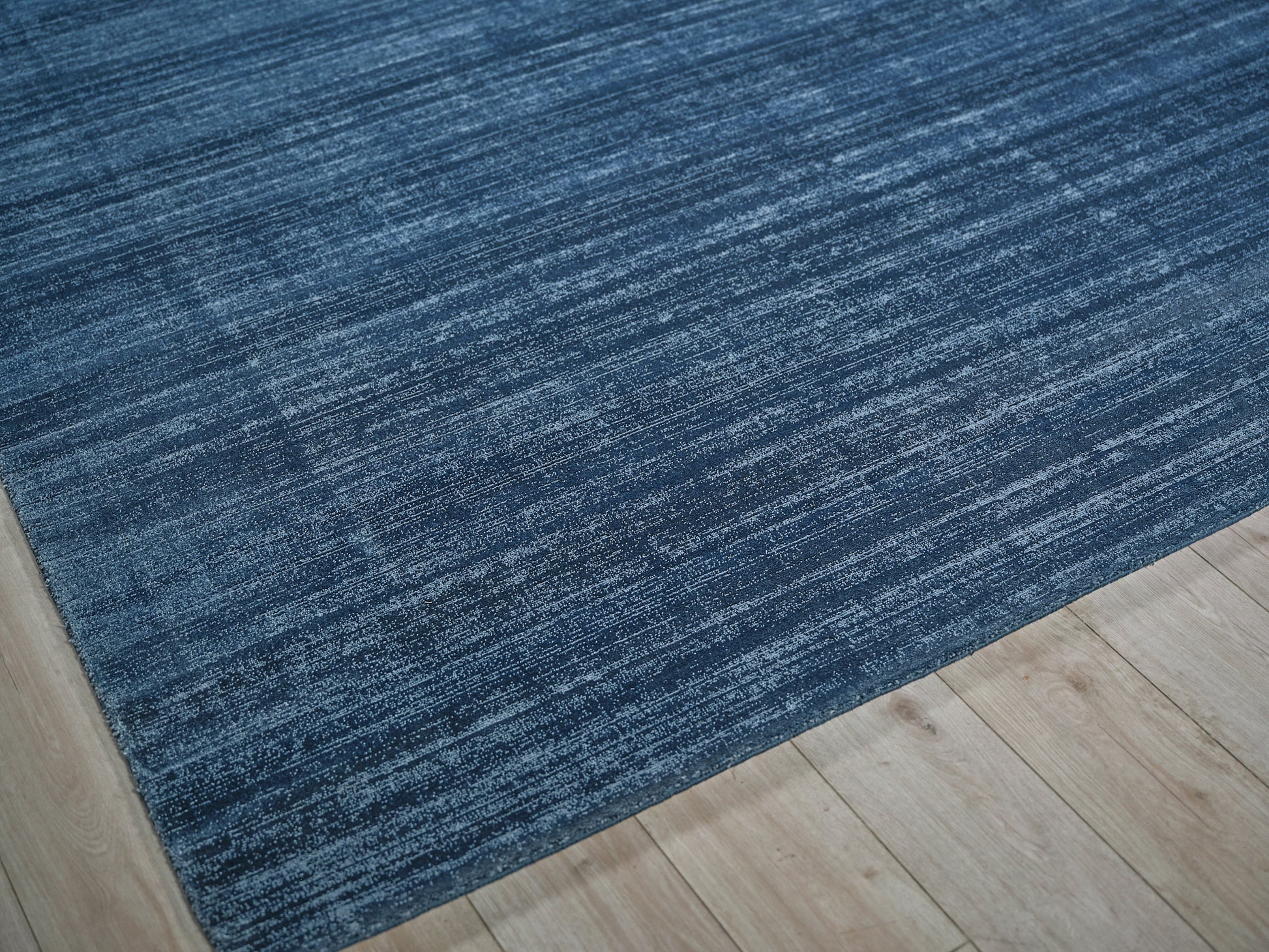 Blue textured hand loomed rug on light wood floor, rectangular area rug.