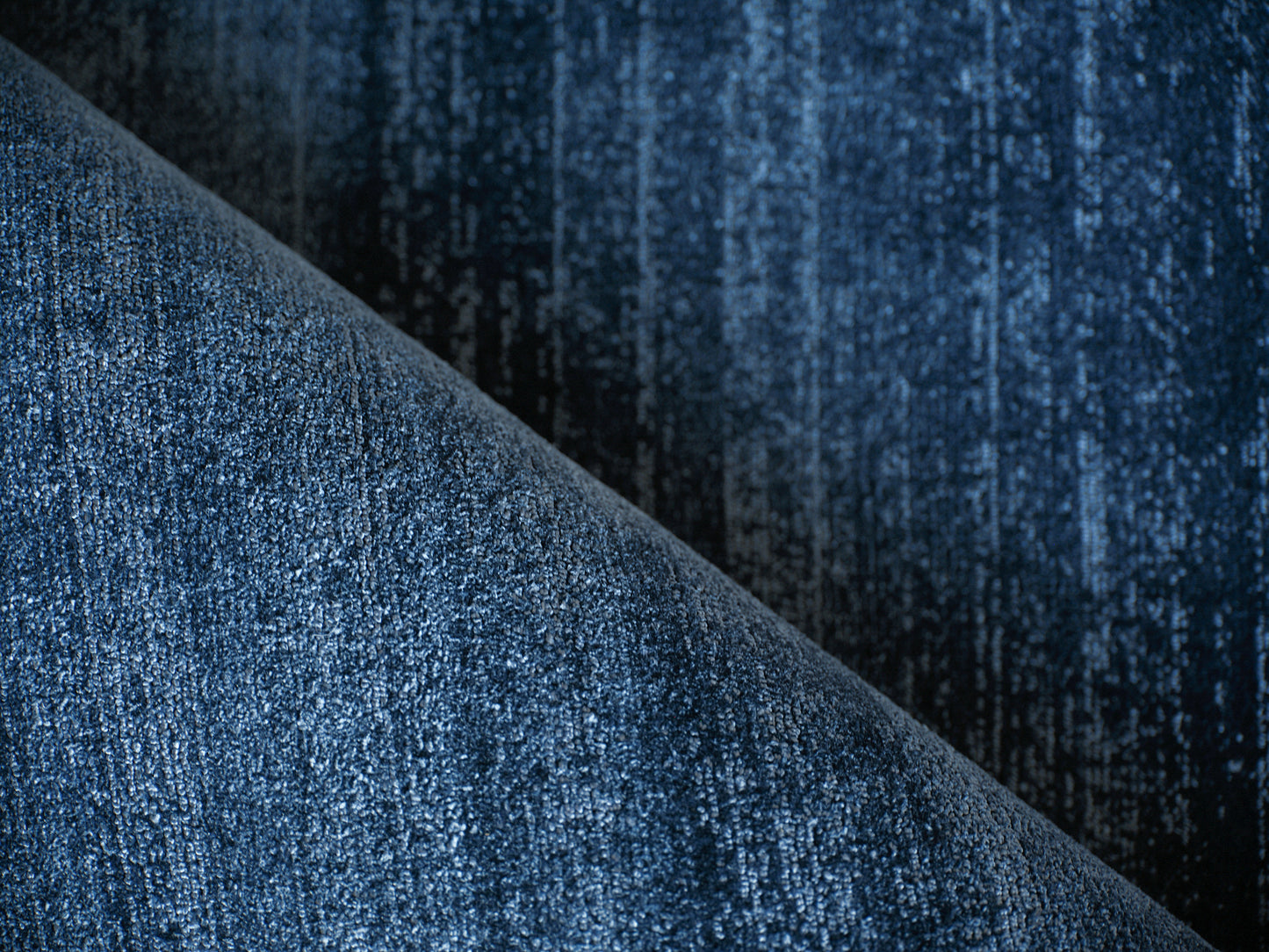 Close-up of dark blue rug fabric with diagonal fold and textured weave.