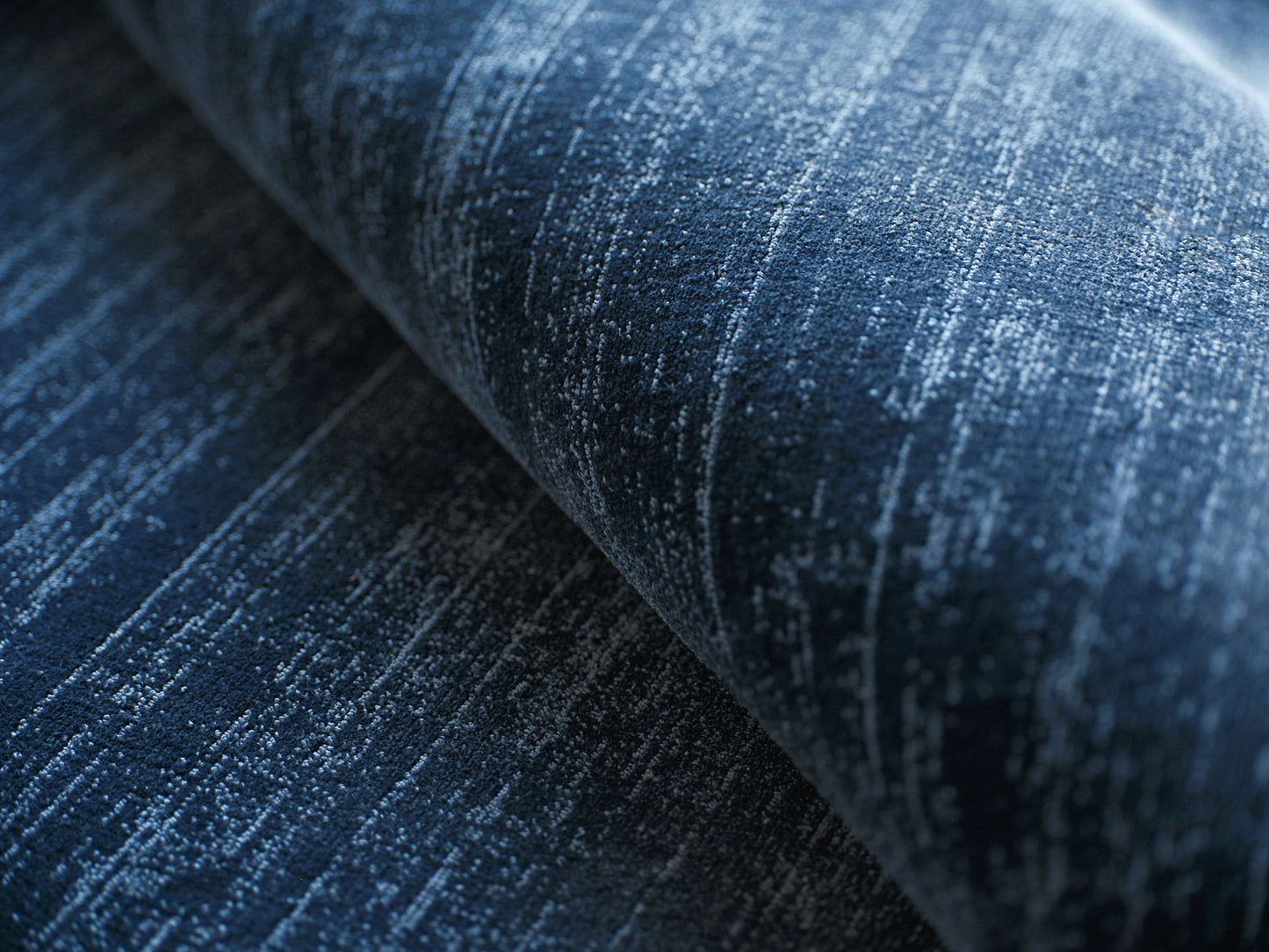 Blue denim-colored rug with a textured weave and light white streaks, rolled to show depth.