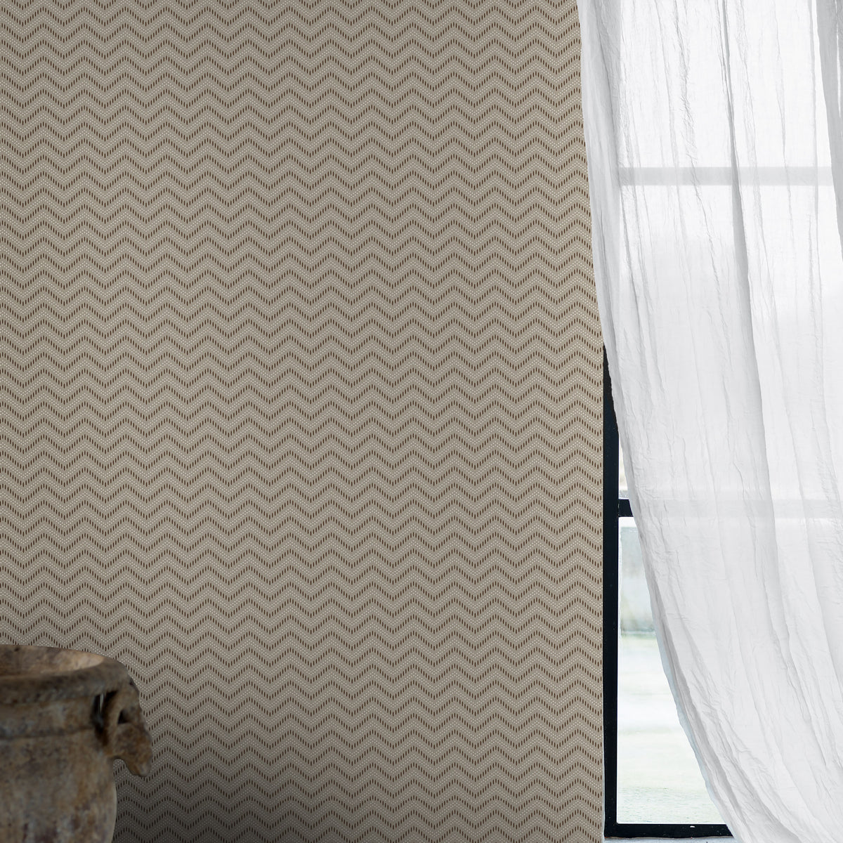 Beige chevron-patterned wallpaper with sheer white curtains by a window; rustic ceramic vase on the lower left.