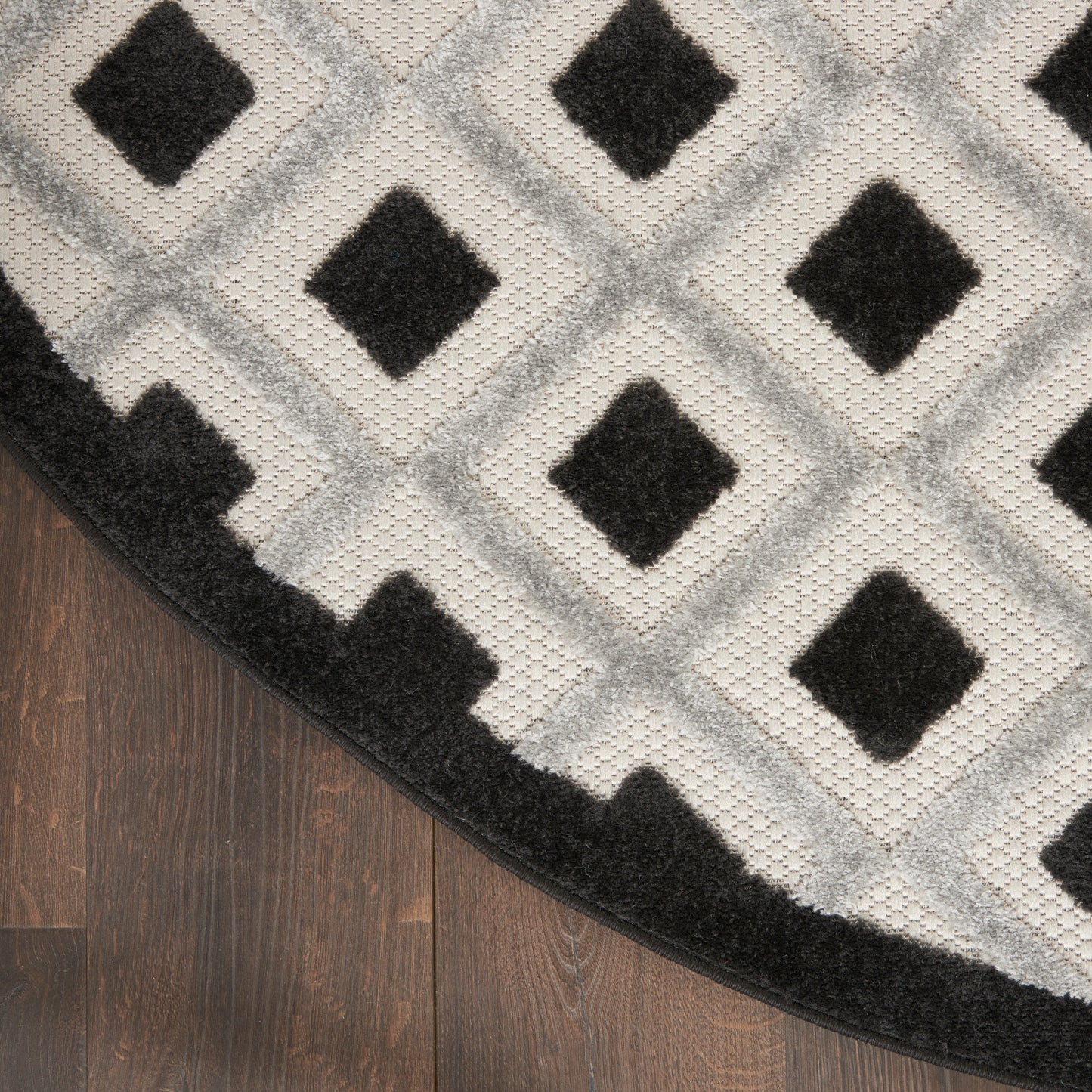 Round plush rug in gray tones with black diamond lattice pattern and a thick black border on wood floor.