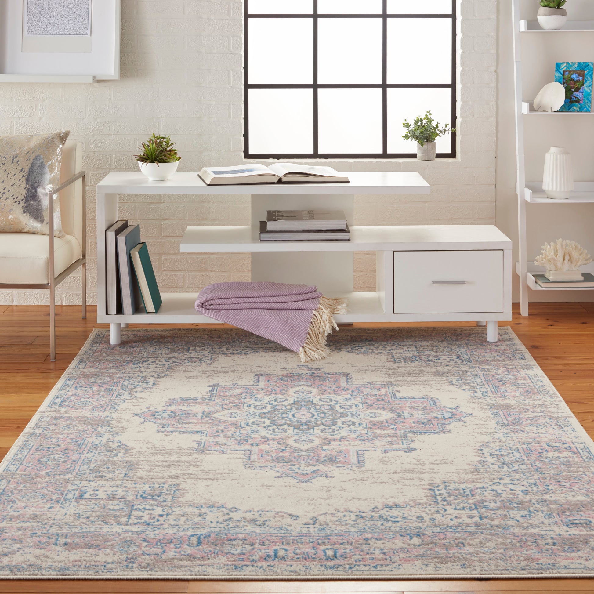 White modern console table with shelf, lavender throw, plant, books; blue-pink rug, brick wall, grid window