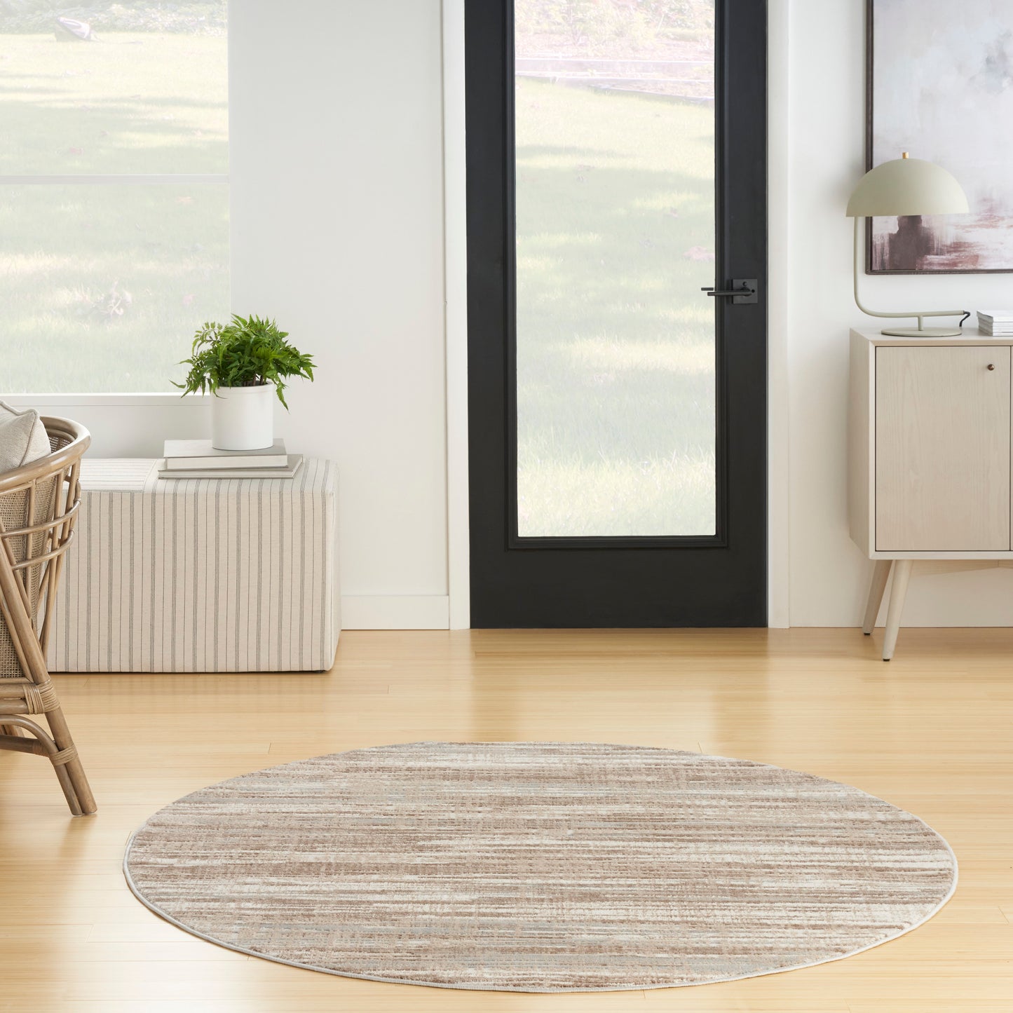 Round beige-striped area rug on light hardwood floor in a modern entryway with a black-framed glass door.