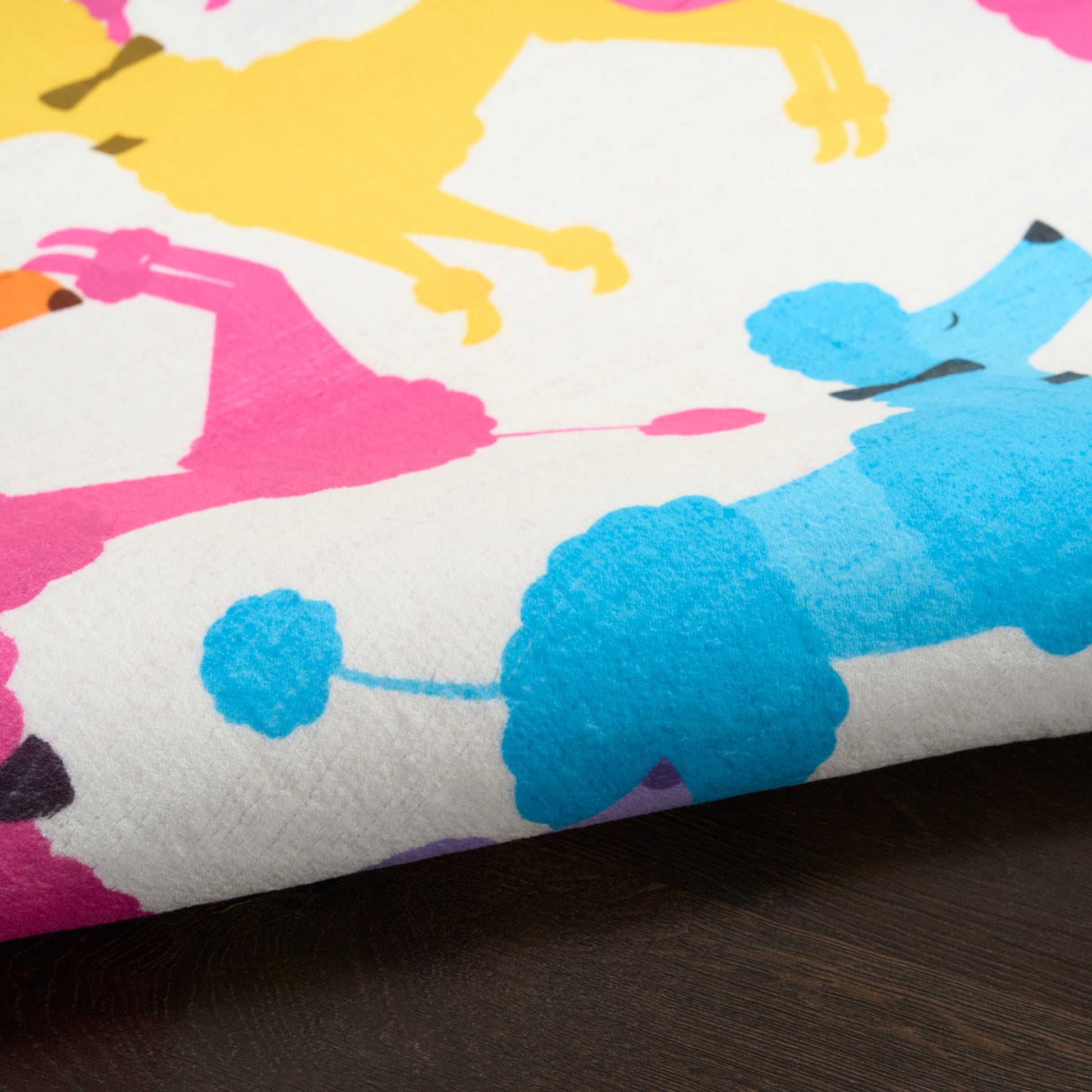 Close-up of a white rug with bright abstract floral shapes in pink, yellow, and blue; soft pile.