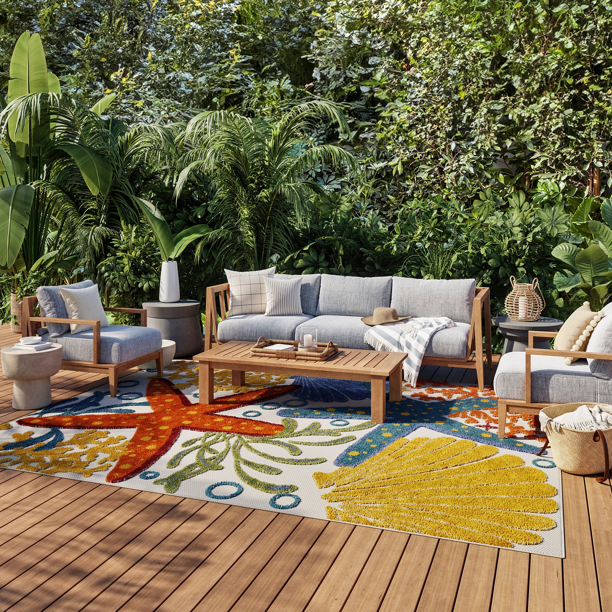 Outdoor patio with blue-cushion sofa and chairs, teak coffee table, and vibrant tropical rug amid lush greenery.