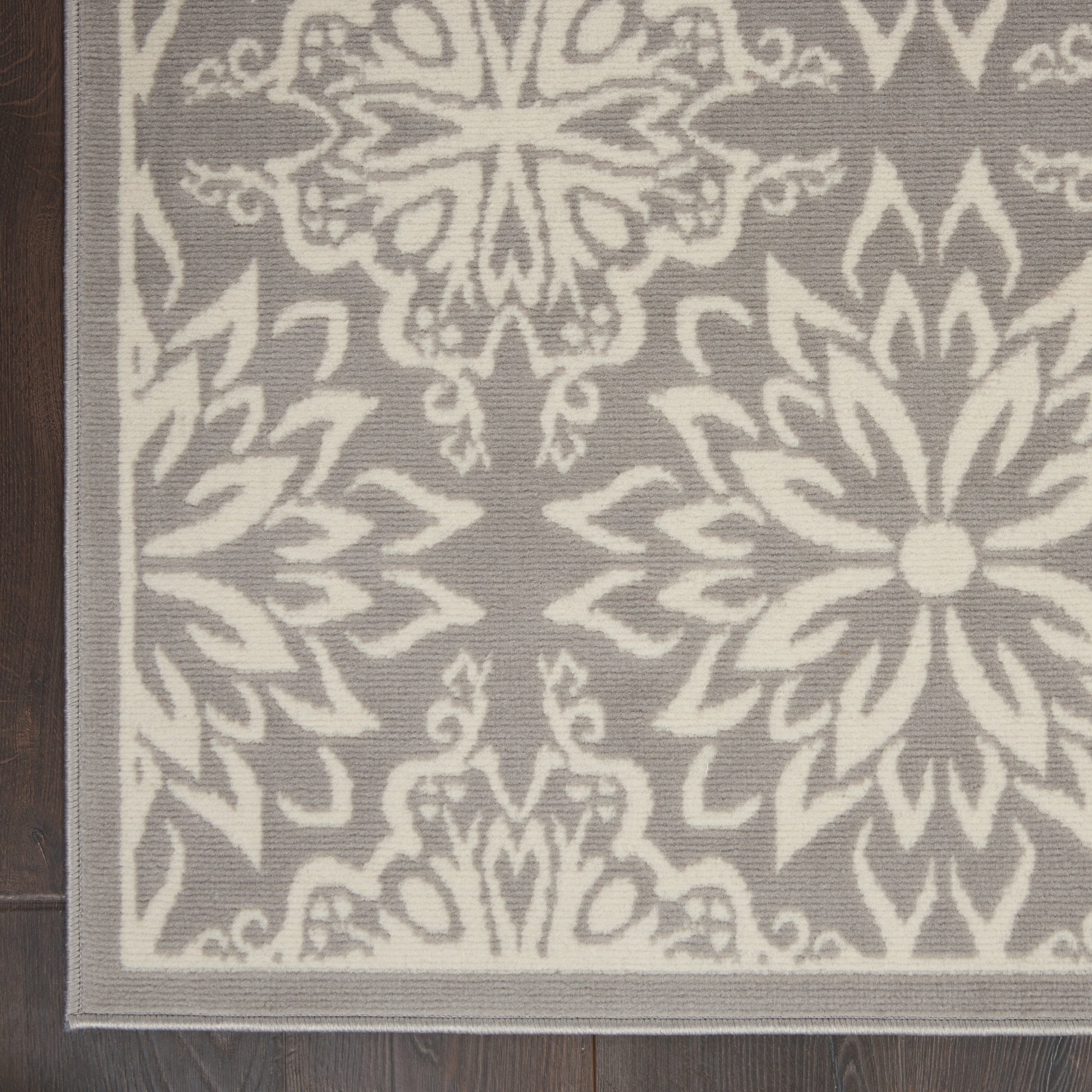 Grey area rug with ivory damask medallions and a light border on dark wood floor.