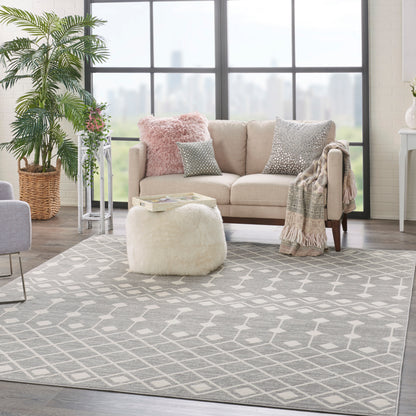 Bright living room with beige sofa, pink fuzzy pillow, gray geometric rug, round cream ottoman, throw blanket, and plants.