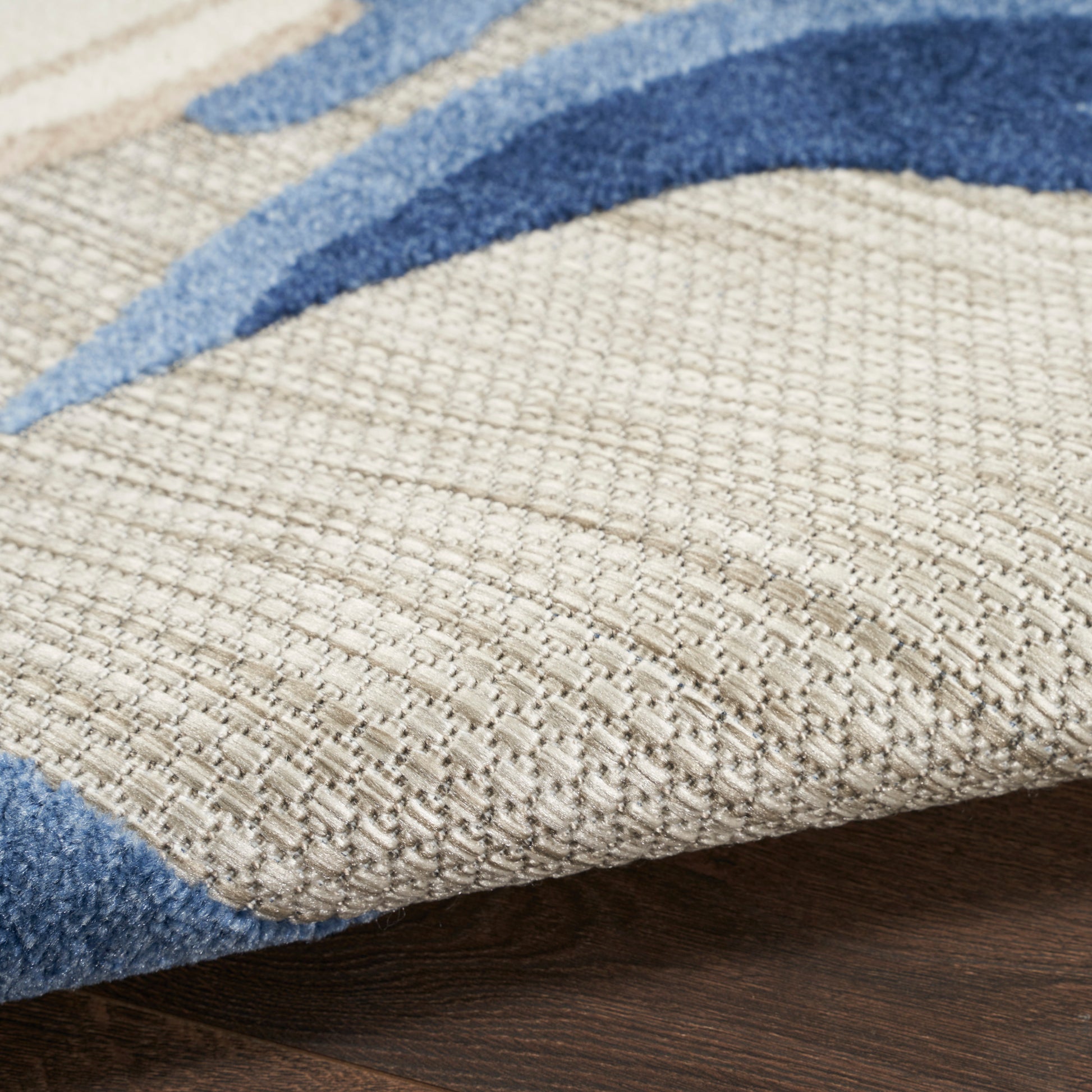 Beige textured woven area rug with navy blue curved stripes on wood floor.