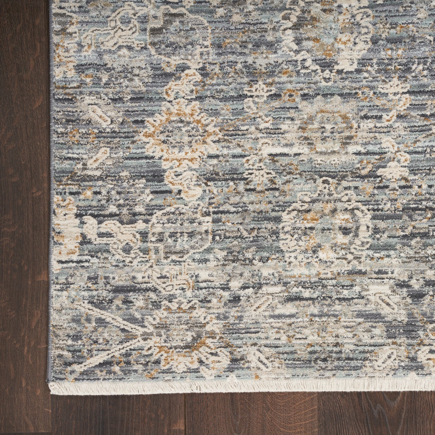 Blue-gray woven area rug with ivory and tan floral damask pattern and fringe edge.