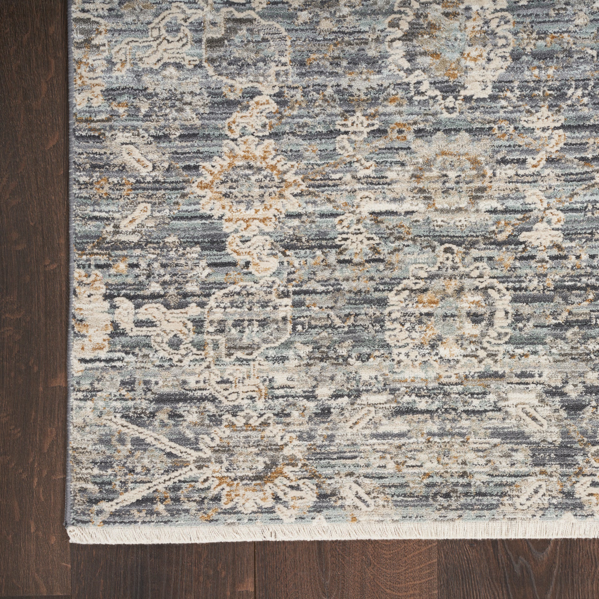 Blue-gray woven area rug with ivory and tan floral damask pattern and fringe edge.
