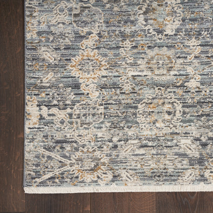 Blue-gray woven area rug with ivory and tan floral damask pattern and fringe edge.