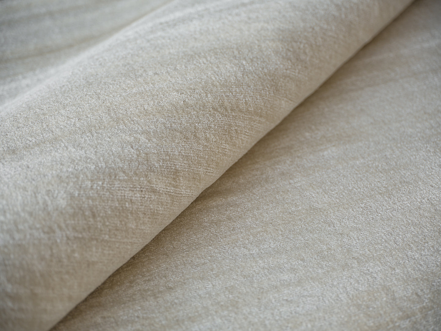 Beige hand-loomed rug with soft nap and subtle sheen, rolled for display; indoor use, 6' x 9'.