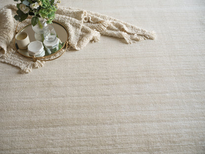 Beige textured rug with round gold-trim mirrored tray, candles, marble candle holder, glass vase, and cream fringe blanket.