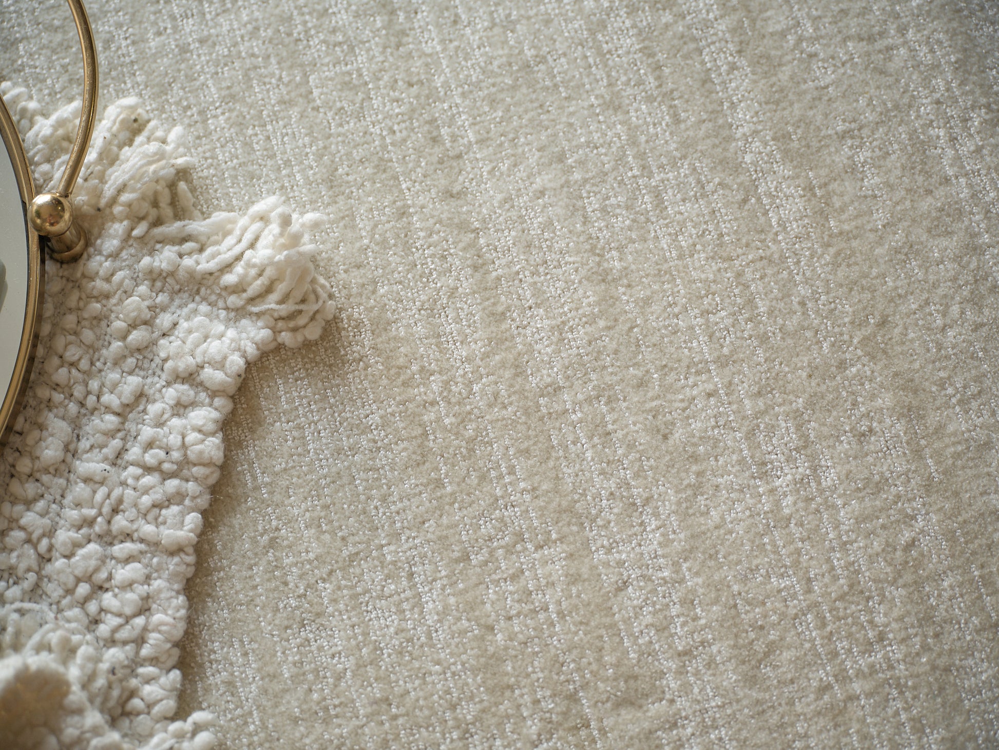 Beige textured rug with cream shag fringe; partial gold round vanity mirror visible on the left