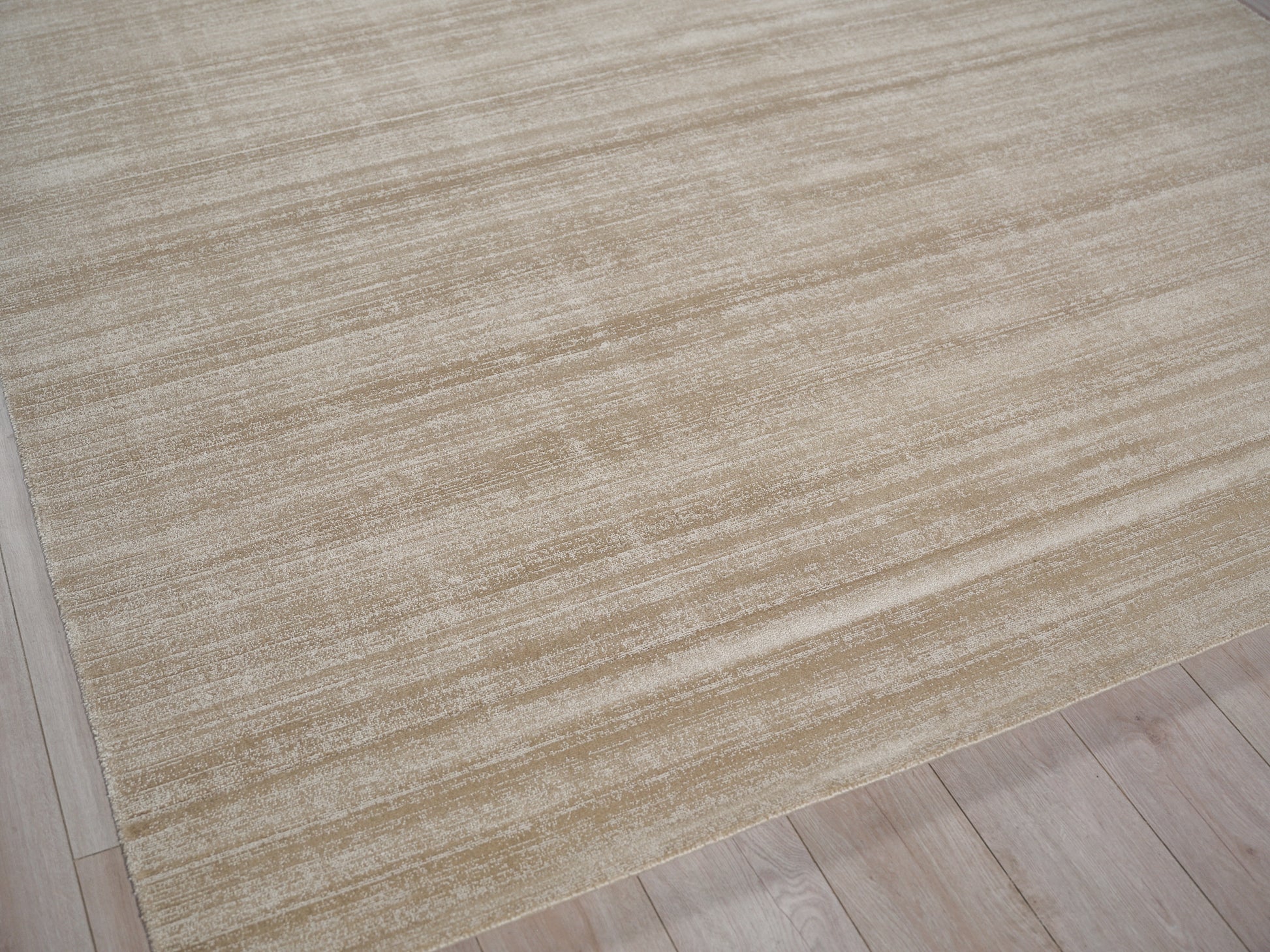 Beige textured area rug with subtle cream stripes on a light wood floor.